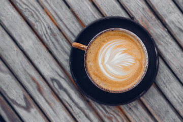 Top view on stylish latte coffee mug with flower art on wooden table background 
