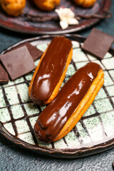 Plate with tasty chocolate eclairs on dark color background, closeup