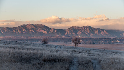 Sunrise over a frost covered field in the foreground of Boulder, Colorado and the Flatirons