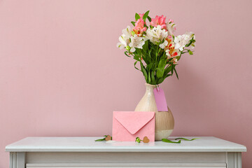 Vase with beautiful alstroemeria flowers and envelope on table near color wall. Mother's day...
