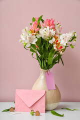 Vase with beautiful alstroemeria flowers and envelope on table near color wall. Mother's day celebration