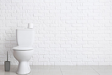 Modern toilet bowl near white brick wall