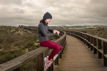 Fototapeta na wymiar Female runner resting and checking her fitness tracker watch after running on a boardwalk.