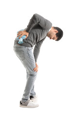 Young man warming his lower back with hot water bottle on white background