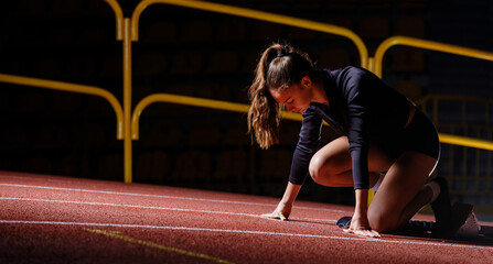 Young sportswoman at the starting blocks before running sprint. Young determined girl at the start of challenge in athletics
