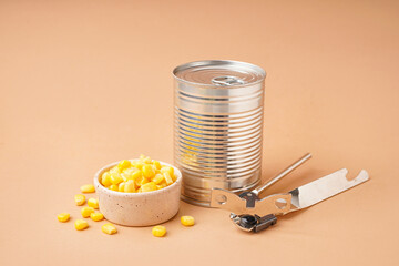 Tin can, bowl with corn kernels and opener on beige background