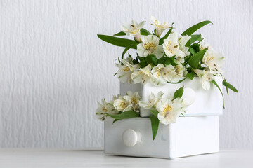 Fototapeta na wymiar Drawers with beautiful alstroemeria flowers on table near light wall