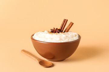 Bowl with delicious rice pudding, cinnamon, anise and spoon on beige background