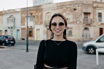 Close up outdoor portrait of brunette smiling woman with dark hair and wonderful smile wearing black top posing at camera on background of summer city