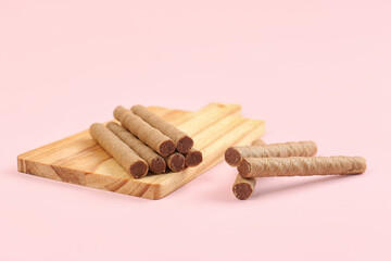Board with tasty wafer rolls on pink background
