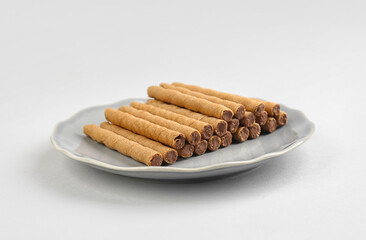 Plate with heap of tasty wafer rolls on grey background