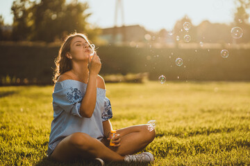 woman sitting on the grass and making soap bubbles