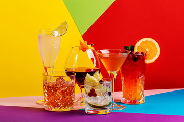 Summer alcoholic cocktails in glasses with rum, gin, prosecco and liquors. Modern style still life on trendy bright multi-colored geometric background