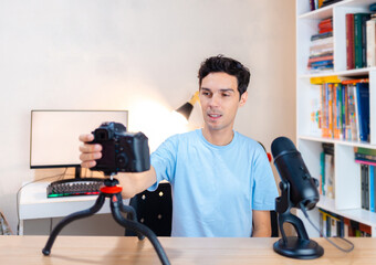 Smiling man influencer having live stream at his home.  Hand pressing the rec button on the camera to start a video recording or to start a live stream