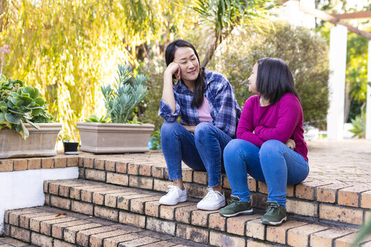 Happy asian mother and daughter talking and sitting on stairs in garden