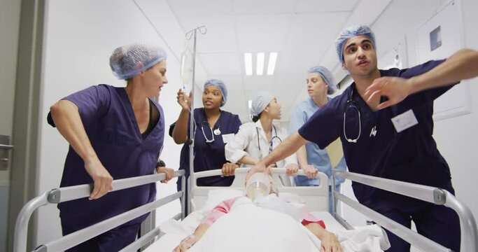 Video of diverse group of medical workers moving patient on ventilator and drip down corridor in bed