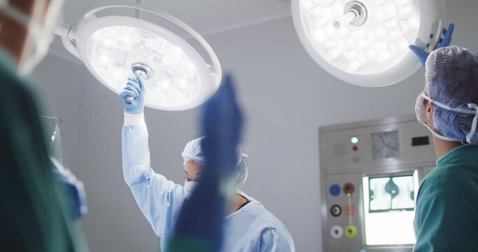 Video of diverse male and female surgical assistants adjusting lights in operating theatre