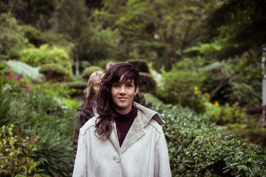Girl with long wavey hair and warm jacket walks through garden smiling