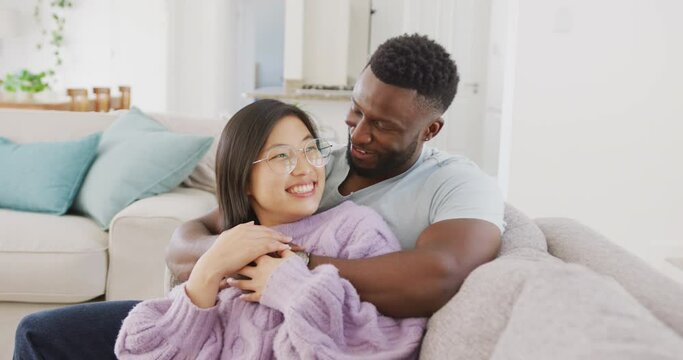Diverse couple sitting on couch and embracing in living room
