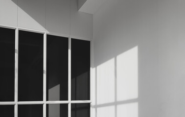 Sunlight and shadow on surface of black tinted glass with white cement wall of office building in...