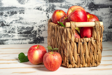 Fototapeta na wymiar Wicker basket full of ripe apples on a white wooden table. Close-up, space for text.