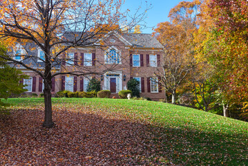 Suburban brick House among autumn trees. Large manicured lawn and landscaping.