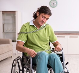Young male invalid in wheel-chair suffering at home