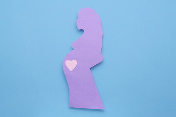 Pregnant woman with heart on belly on light blue background, top view