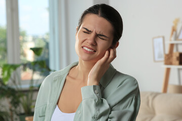 Young woman suffering from ear pain at home
