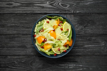 Delicious salad with Chinese cabbage, lemon, persimmon and pomegranate seeds on black wooden table, top view