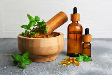 Wooden mortar with fresh green herbs, extracts and capsules on light grey table
