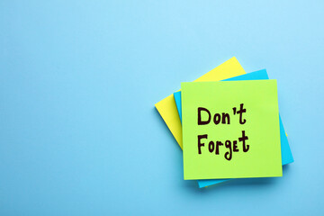 Paper note with phrase Don't Forget on light blue background, top view. Space for text