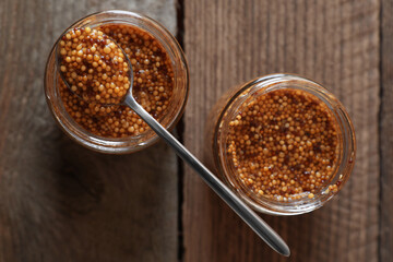 Jars and spoon of whole grain mustard on wooden table, flat lay