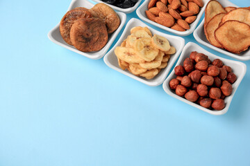 Bowls with dried fruits and nuts on light blue background, space for text
