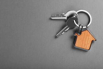 Keys with trinket in shape of house on grey background, top view and space for text. Real estate agent services