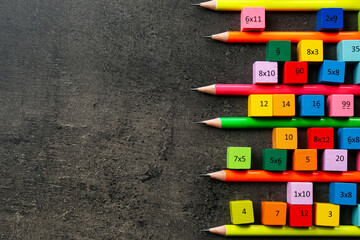 Many colorful cubes with numbers, multiplications and pencils on dark grey table, flat lay. Space...