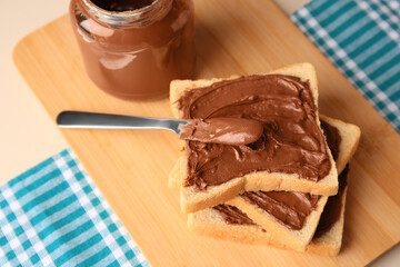 Tasty toasts with chocolate paste and jar of cream on beige table
