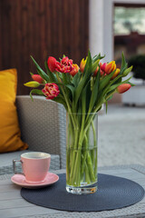 Beautiful bouquet of colorful tulips and cup with drink on rattan garden table outdoors