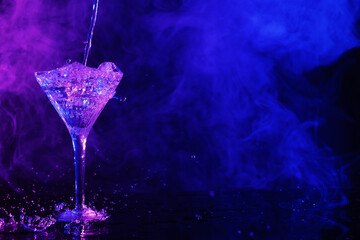 Pouring fresh martini into glass on table in neon lights, space for text