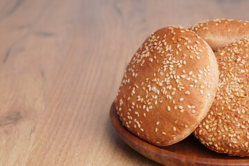 Fresh buns with sesame seeds on wooden table. Space for text