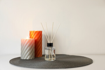 Aromatic reed air freshener and burning candles on white table