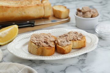 Tasty sandwiches with cod liver and lemon on white marble table