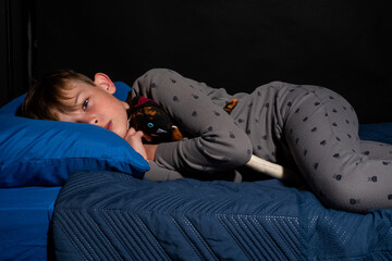 Scared little boy lying awake in bed with his stuffed toy - obrazy, fototapety, plakaty