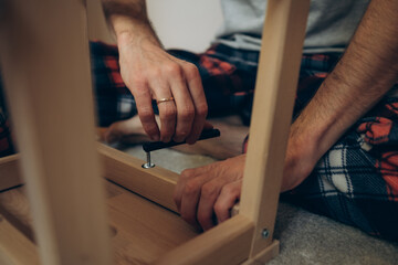 Obraz premium a man collects wooden furniture with his own hands while sitting on the floor in an apartment