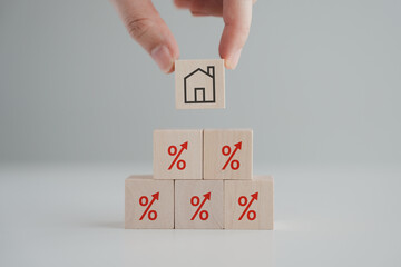 Hand holding house icon on wooden block from red percentage sign with arrow up. Refinance, Interest...