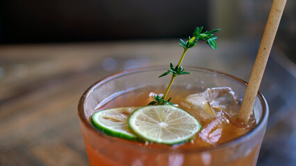 Selective focus a glass of refreshing cold soft drink lemon iced tea in ice cube with paper straw, decorated with sliced lime and thyme branches, summer drink