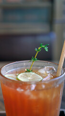 Selective focus a glass of refreshing cold soft drink lemon iced tea in ice cube with paper straw, decorated with sliced lime and thyme branches, summer drink