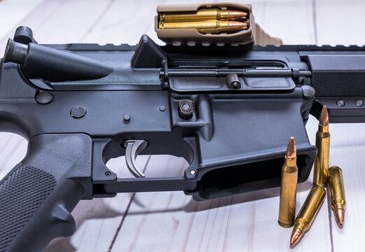 An AR15 rifle chambered in 223 caliber with four bullets and a loaded magazine next to it on a white wooden background