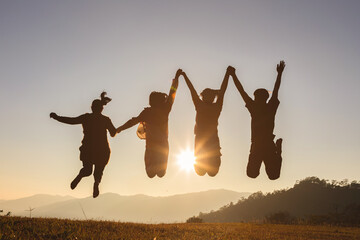 Four people jumping on mountain sunset sky background.