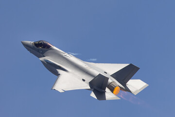 Close side view of a F-35A Lightning II  with afterburner on and condensation streaks